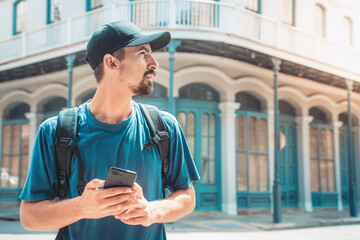 young tourist man with backpack looking smartphone while touring a foreign city, travel vacation