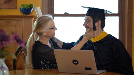 Wall Mural - Closeup of graduating young man switching tassel and holding diploma giving a thumbs up as mother smiles and watches him.