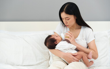mother feeding milk bottle to her newborn baby on bed