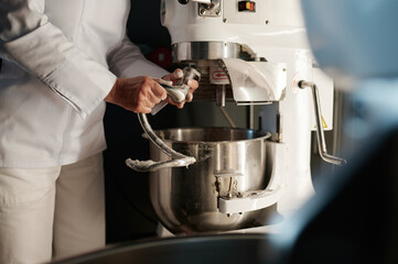 Female baker working in professional kitchen with dough mixer at bakery