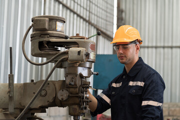 Wall Mural - Male factory worker working at work maintenance machine in industrial factory while wearing safety uniform, glasses and hard hat. Caucasian male technician and heavy steel lathe machine in workshop