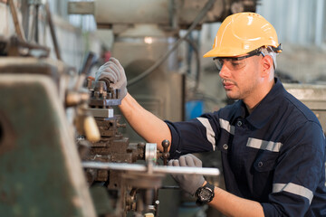 Wall Mural - Male factory worker working at work maintenance machine in industrial factory while wearing safety uniform, glasses and hard hat. Caucasian male technician and heavy steel lathe machine in workshop