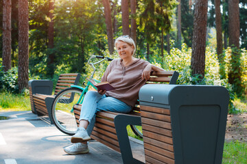 Dreamy modern old lady relaxing in city park. Pensive senior grey haired woman in casual sitting wooden bench outdoors.