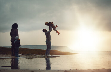 Sunset, view and a playing family on the beach together on a beautiful summer evening outdoor. Earth, water or nature with a mother, father and children bonding by the ocean or sea at the coast