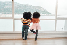 View, Back And Children Looking From A Window For Play, Beach And Childhood Together. Indoors, Standing And Kids Waiting In A House To Visit The Sea On A Vacation Or Holiday At The Ocean For Playing