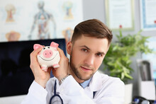 Portrait Of Male Doctor Holding A Piggy Bank On Voluntary Donations Of Money For A Hospital Or Clinic