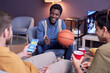 © Seventyfour - Diverse group of sports fans watching basketball match at home and using online betting app