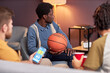 © Seventyfour - Side view at diverse group of sports fans watching basketball match at home and using online betting app