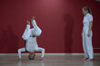 © afefelov68 - A mature man, a sports master, and a young woman, an aspiring athlete, practice the Brazilian martial art of capoeira in a small gym.