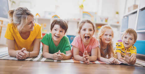 Wall Mural - Group of children and teacher lying on the floor and looking in the camera.