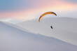 A paraglider is planning in the sky in a hilly area.