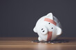 Financial problem, Bankrupt or fail in business concept. White piggy bank with plastic adhesive bandages on wooden desk with dark copy space wall background. Fail, Bankrupt or unsuccessful idea.