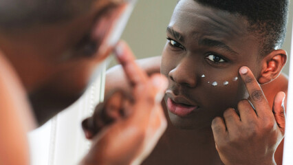 Facial cream. Skin treatment. Anti-aging skincare. Closeup of man applying under eye face moisturizing cosmetic product in mirror reflection.