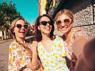 Wall Mural - Three young beautiful smiling hipster female in trendy summer dresses clothes. Sexy carefree women posing in the street. Positive models having fun, talking, chatting. Going crazy. Taking selfie