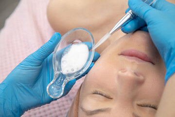 Cropped cosmetologist hands in blue gloves applying white benzoyl peroxide powder with spatula, facial chemical cream