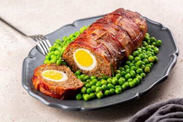 Wall Mural - Baked meatloaf made of ground meat, onion, carrot, stuffed with hard-boiled eggs, wrapped with bacon net, served with green peas. German, Scandinavian and Belgian dish. Festive and Easter food.