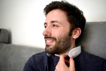 Happy caucasian man sitting on the sofa while wearing neck pain relief device