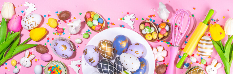 Wall Mural - High-colored Easter baking background, Easter sale, party invitation flaylay, Colorful Easter eggs, chocolate eggs and bunny rabbit with sugar sprinkles on bright pink background top view copy space