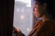 © Johnér - Young woman using phone by window