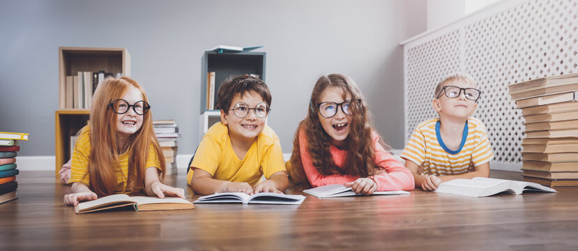 Fototapete - Four cute children in glasses lying on the floor indoors with books