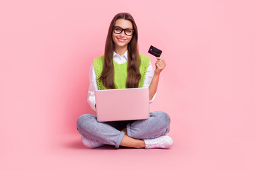 Sticker - Full size photo of charming positive woman wear green waistcoat jeans sneakers laptop on legs hold card isolated on pink color background