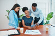 © Meeko Media - Black business woman sits and shows standing colleagues report on digital tablet