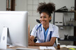 © Parichat - Portrait of female African American doctor sitting in her office at clinic. working with dewsktop computer.