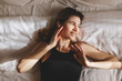 © zvkate - Beautiful young woman listening music in wireless headphones at home lying on bed. Woman person are happy and enjoy with music by using earphone for listen a sound audio in bedroom look at side.