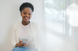 © Strelciuc - Portrait of attractive young African American woman with afro hair wearing white jacket reading messages on the phone sitting in a cafe. Online communication