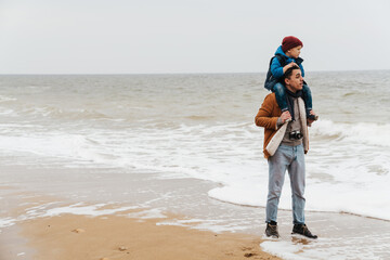 Wall Mural - Father carrying on shoulders his son while walking together on beach