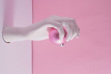 Creative Arrangement With Artificial Woman's Hand Reaching Out Of A White Wall Holding Pink Christmas Decoration. Pastel Background. New Year Evening Composition.