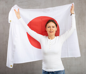 Cheerful adult woman holding big Japan flag in her hands