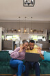 © Wavebreak Media - Happy african american couple sitting on sofa and using laptop for video call in living room