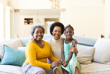 Portrait Of Happy African American Grandmother, Mother And Daughter Sitting On Sofa In Living Room