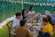 Group of Asian people eating food and drinking wine together during outdoor celebration dinner party in the garden on summer holiday vacation. Man and woman friend reunion dining meeting at restaurant