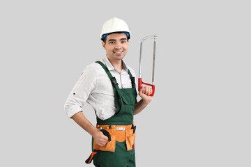 Poster - Young carpenter with hacksaw and hammer on grey background