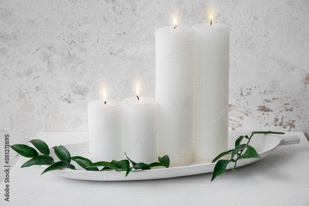 Burning candles and ruscus branch on table near grey grunge wall