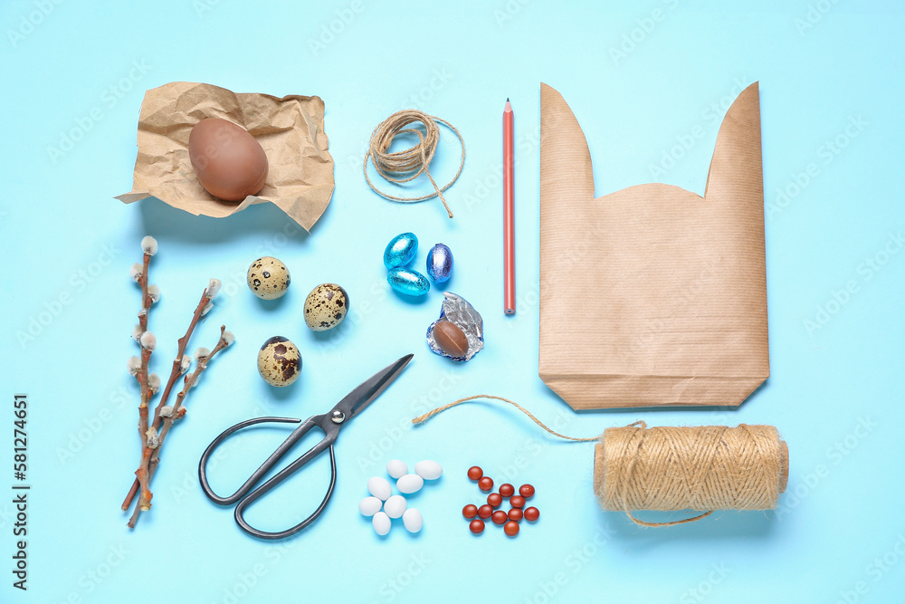 Composition with bunny gift bag, Easter eggs, candies and scissors on blue background