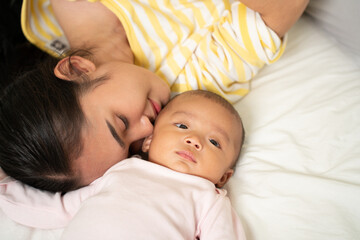 loving asian mom carying of her newborn baby at home in the bedroom. happy family. mother playing wi