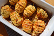 Hasselback baked Potatoes with fresh herbs and garlic in a white baking dish. Traditional swedish food