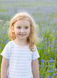 © Kufotos - A little girl in a dress and with curly hair smiles in a field with cornflowers on a summer day.