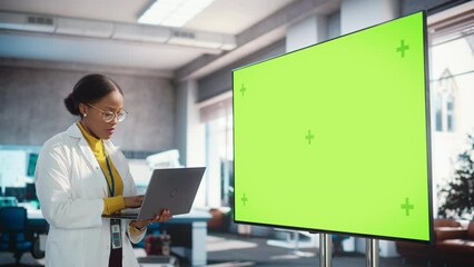 Poster - Portrait of Young Black Woman Working in a Lab of Industrial Startup. Female Specialist Using a Laptop Computer and Looking at a Green Mock Up Displayed on Big Digital Screen. Screen Replacement