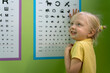 © somemeans - Cheerful little girl at appointment with optometrist near poster to check her eyesight. Pediatric optometrist.