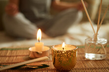Close-up Of Scented Candle, Diffuser. A Woman Sits In A Lotus Position, Meditates.