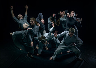 Wall Mural - Group of young men and women contemp dancers performing against black studio background. Concept of modern freestyle dance, contemporary art, movements, hobby and creative lifestyle