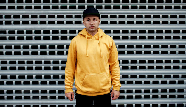 city portrait of handsome guy wearing yellow blank hoodie or sweatshirt and black baseball cap with 