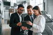 © standret - Standing and reading information in the graphic tablet. Three people are working together in the car showroom