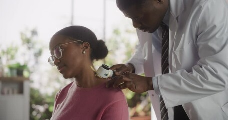 Wall Mural - Portrait of a Black Dermatologist Using a Medical Magnifying Glass to Inspect any Damages on the Skin of a Female African Patient During a Health Check Visit to a Clinic. Doctor Working in Hospital