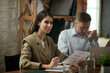 © master1305 - Young woman, project manager in formal wear sitting at table during business meeting in office. Team leader. Checking documents. Concept of business, teamwork, career development, brainstorming