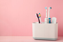 Holder with modern electric toothbrushes and manual toothbrushes on pink background